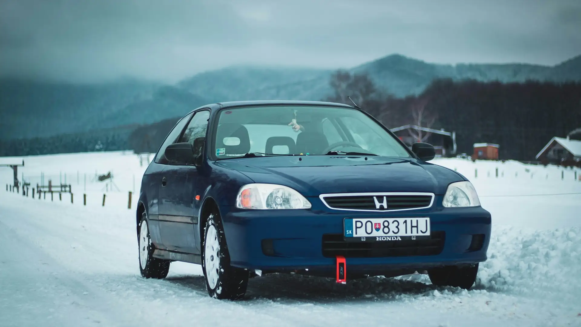A blue Honda Civic in the snow, mountains behind it