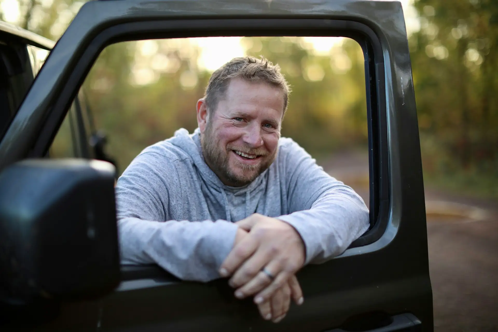 A smiling man leaning on the open door of his truck