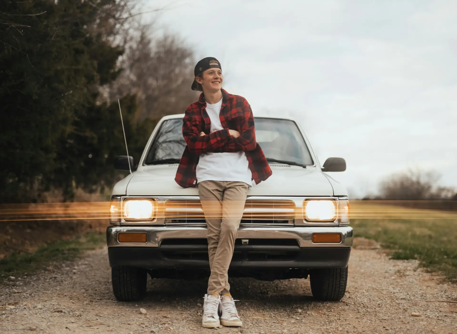 A young man leaning on the front of his pickup truck
