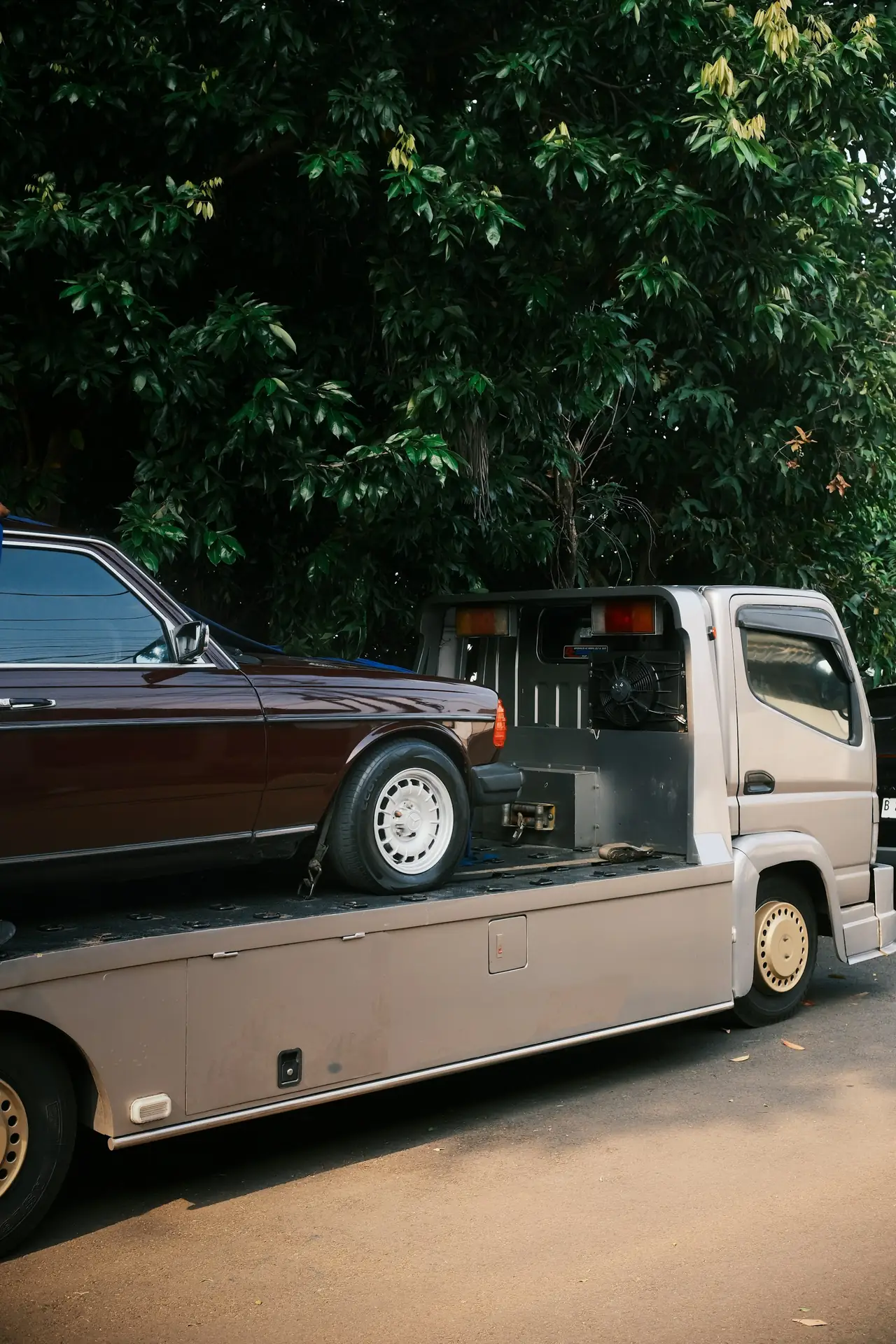 An old sedan strapped onto a flatbed tow truck