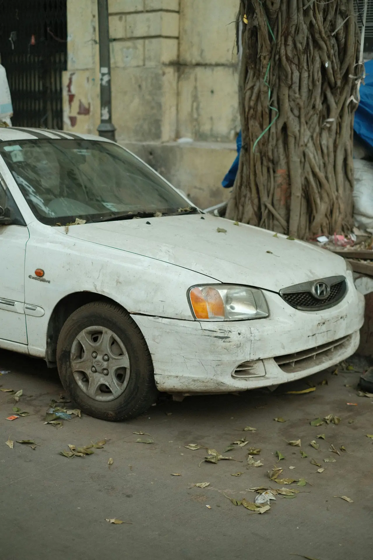 A white Hyundai Accent with a dented front, parked on the street