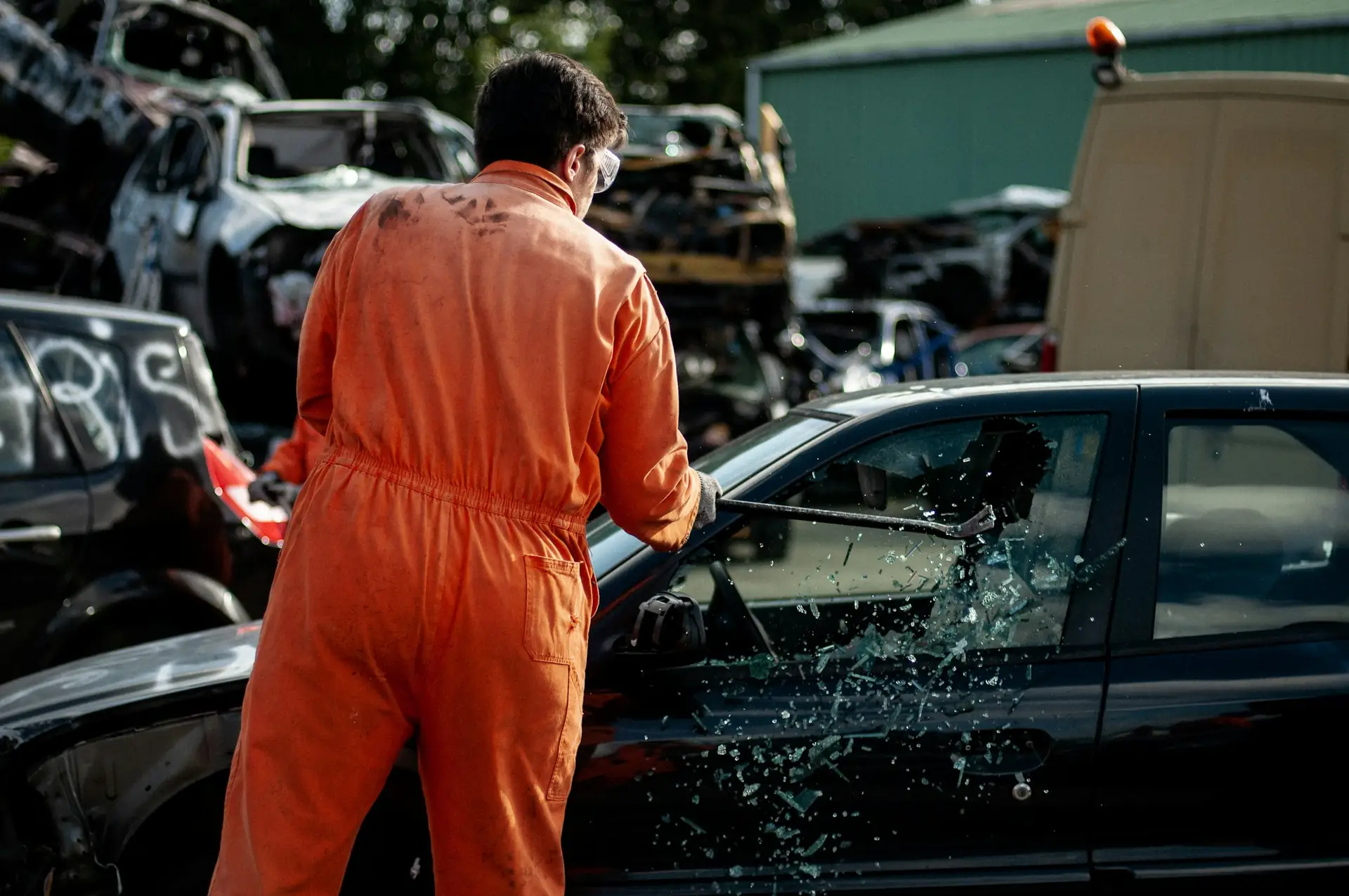 A recycling yard worker in orange coveralls working on a car