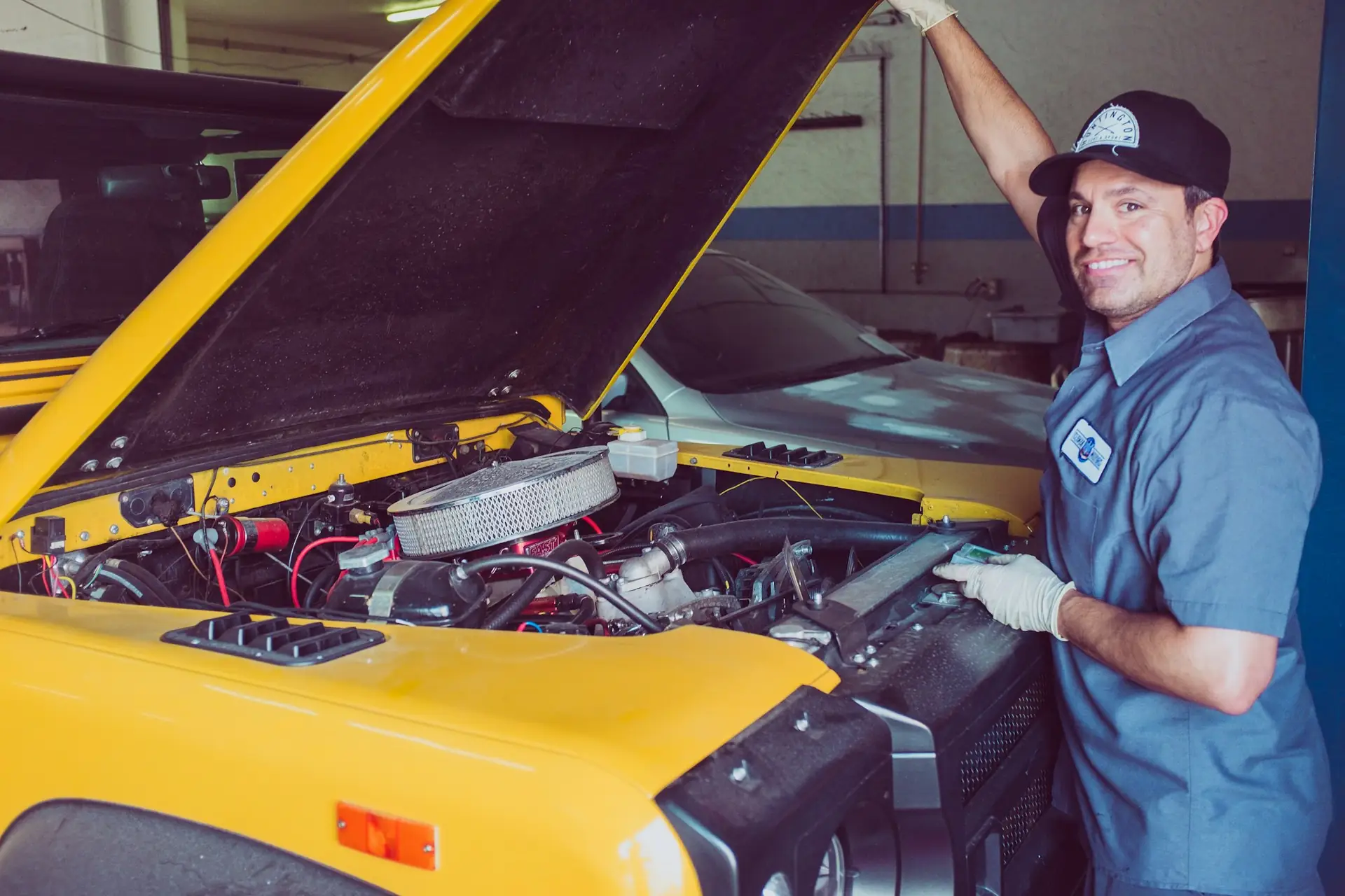 A smiling mechanic working under the hood of a yellow car