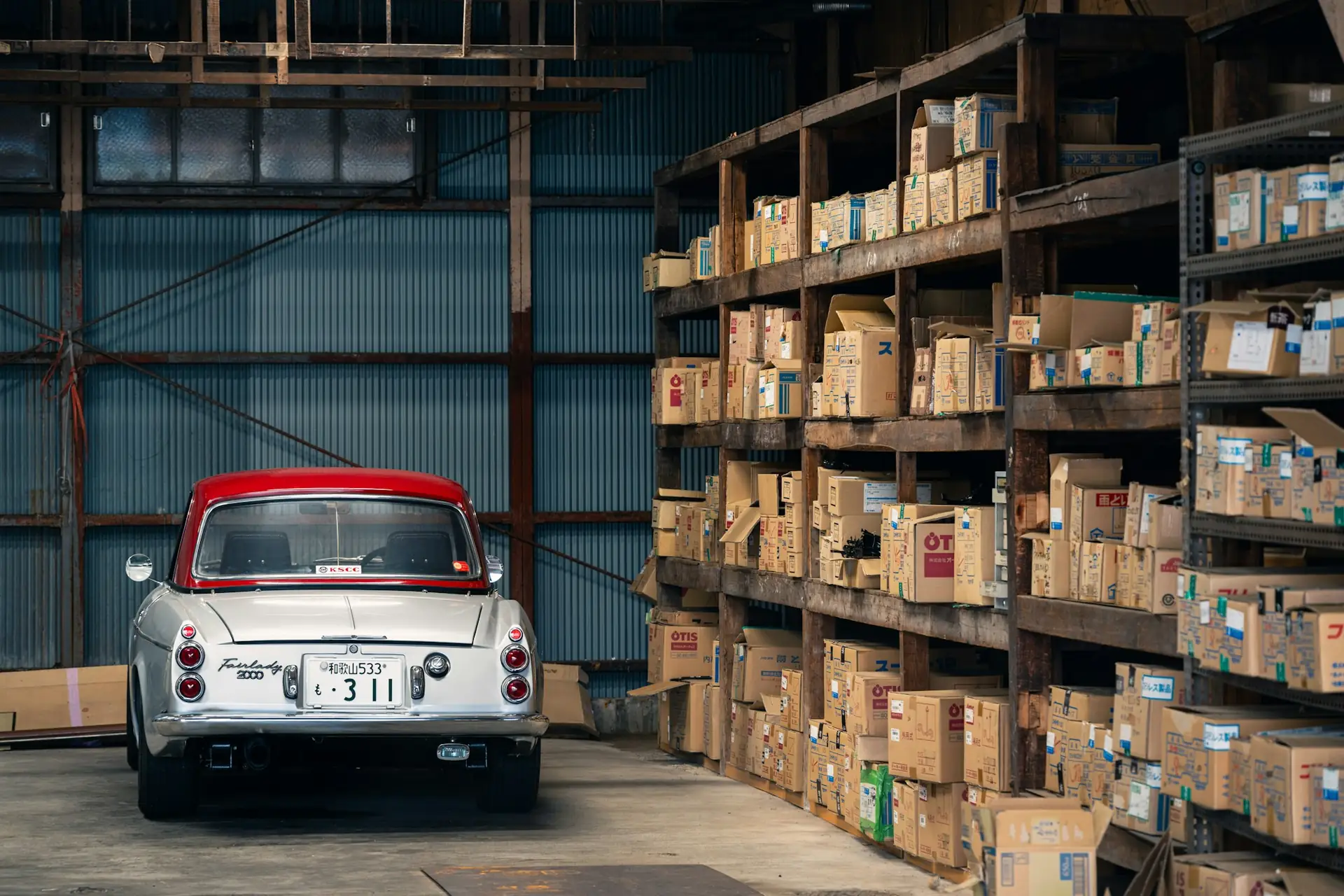 A parts warehouse with shelves of boxed car parts and a classic car