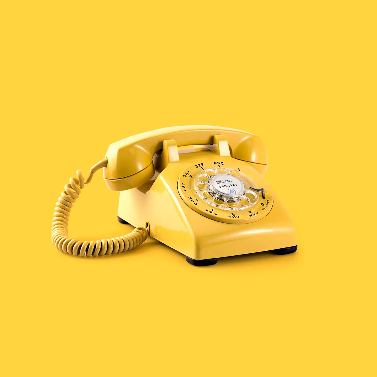 A yellow rotary phone on a yellow background