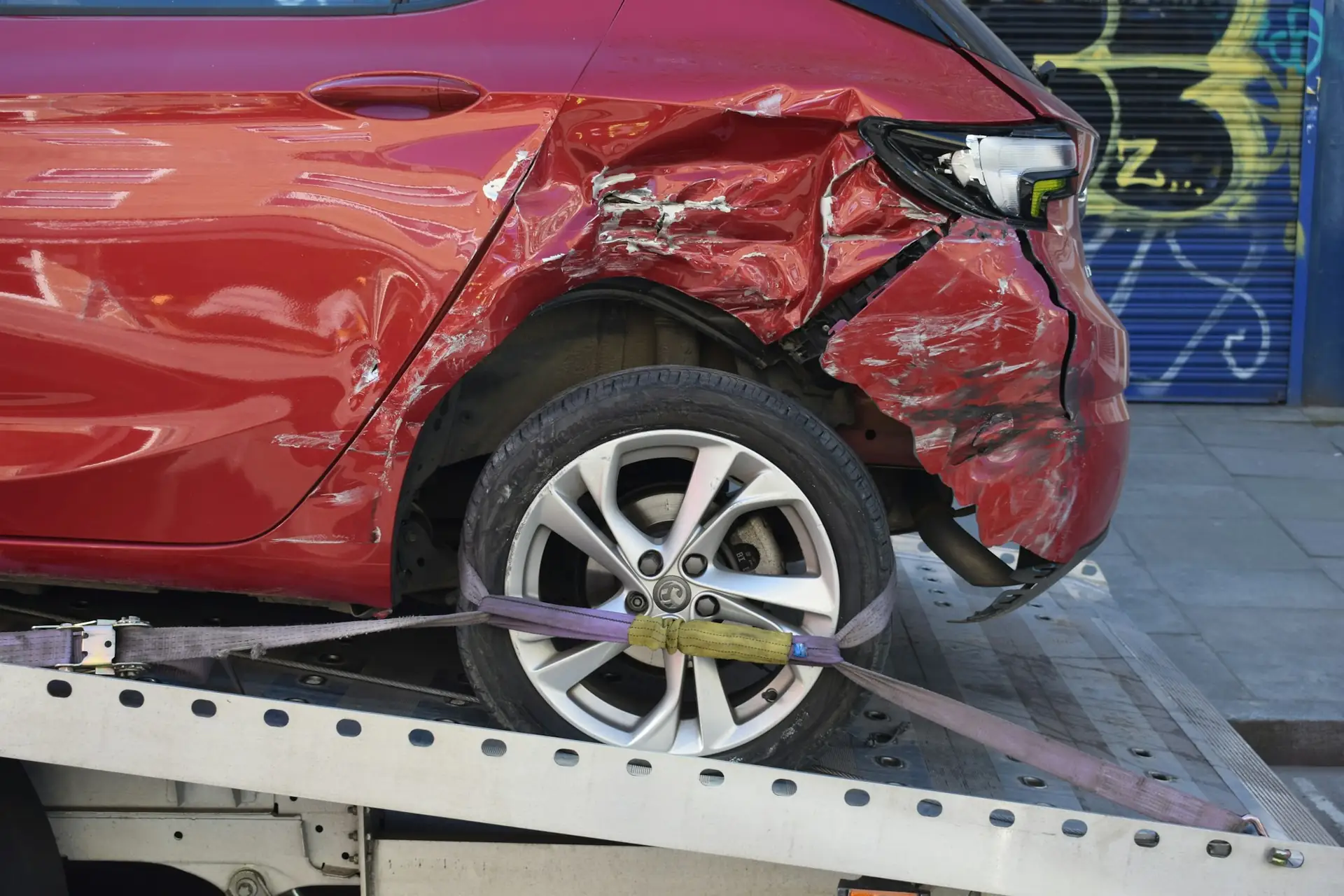 A damaged red car strapped onto a flatbed tow truck